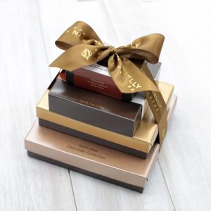 Four boxes stacked vertically from largest to smallest. They are tied together with a brown bow that reads John Kelly Chocolates.